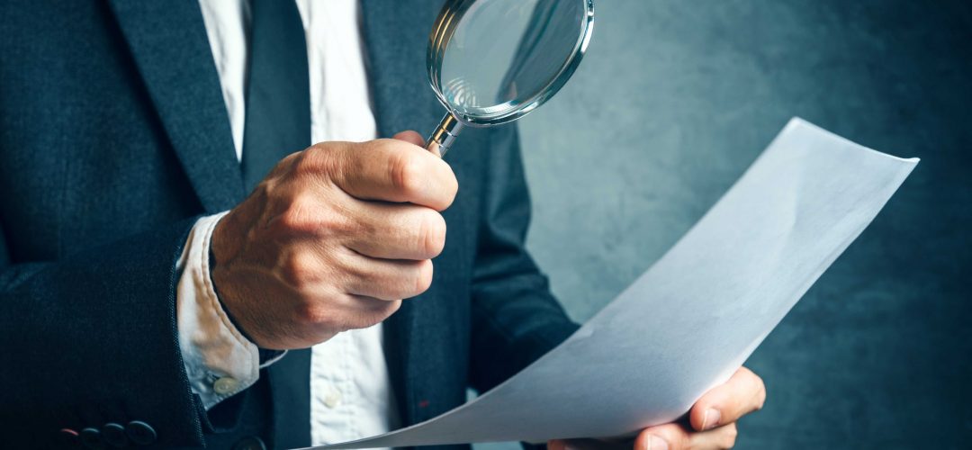 Tax inspector investigating financial documents through magnifying glass, forensic accounting or financial forensics, inspecting offshore company financial papers, documents and reports.